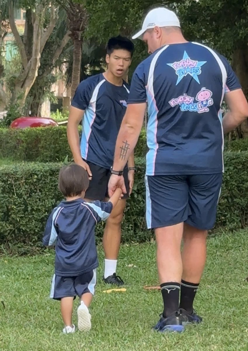 Toddler holding a Rugbytots coach's hand on the grass